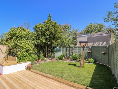 A backyard with grass lawn wooden deck fence trees and plants at Towyn Hall in New Quay