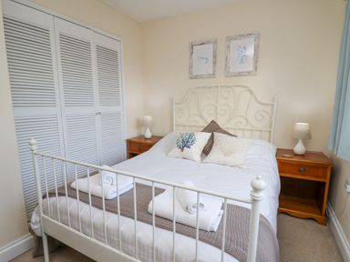 A bedroom with a white metal bed frame two bedside tables with lamps and folded towels on the bed at Towyn Hall in New Quay