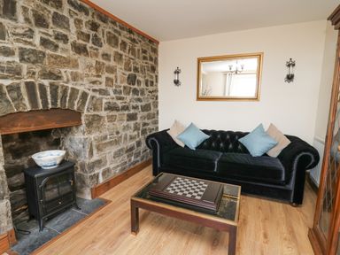 A sitting room with a stone fireplace a black sofa with cushions and a coffee table with a chessboard at Towyn Hall in New Quay
