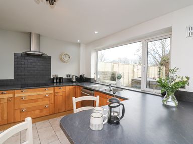 A kitchen with wooden cabinets a black countertop a stove a coffee press mugs a clock and a window at Towyn Hall in New Quay