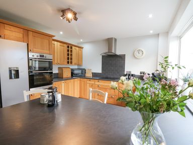 A kitchen with wooden cabinets a refrigerator an oven a microwave coffee mugs and a vase with flowers on a countertop at Towyn Hall in New Quay