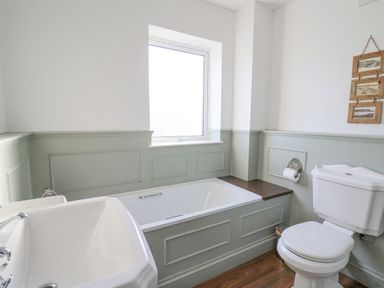 A bathroom with a bathtub under a window a sink and a toilet at Towyn Hall in New Quay