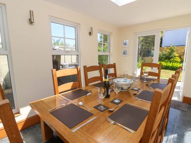 A dining room with a wooden table set for six with placemats glasses cutlery and a bottle at Towyn Hall in New Quay
