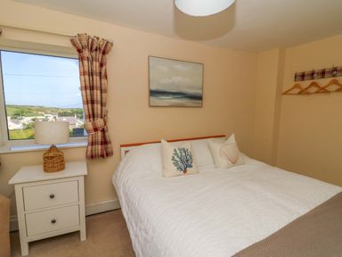 A bedroom with a bed with white bedding and decorative pillows a nightstand with a lamp and a window with plaid curtains at Towyn Hall in New Quay