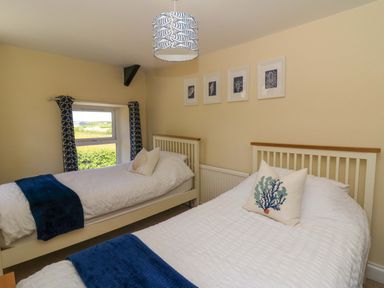 A bedroom with two single beds white bedding blue throws and a window with patterned curtains at Towyn Hall in New Quay