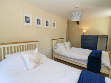 A bedroom with two single beds white bedding cushions framed pictures and a chest of drawers at Towyn Hall in New Quay