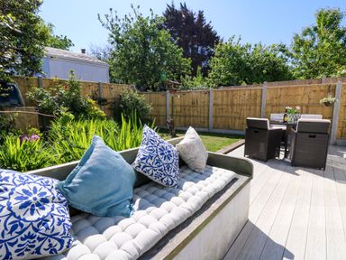 A garden patio with a cushioned bench with patterned pillows and a dining table with chairs at Towyn Hall in New Quay