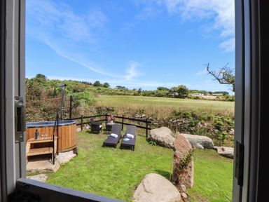 A garden area with two lounge chairs towels a wooden hot tub and a small table with chairs at Bosulla Shepherds Hut in Penzance