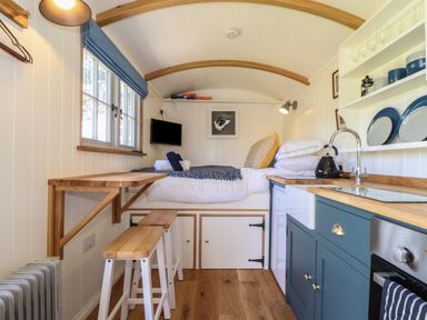 A compact living space with a raised bed a small kitchen and a foldable wooden table at Bosulla Shepherds Hut in Penzance