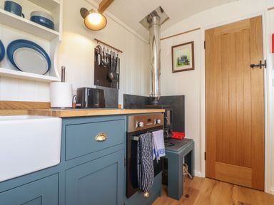 A kitchen with blue cabinets a wooden countertop an oven a wood stove and a wooden door at Bosulla Shepherds Hut in Penzance