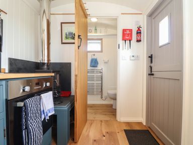 A kitchen area with an oven and stove next to a door leading to a bathroom with a toilet at Bosulla Shepherds Hut in Penzance