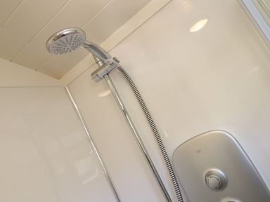 A shower head attached to a wall with a hose and control knob in a bathroom at Bosulla Shepherds Hut in Penzance
