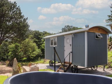 A shepherds hut on wheels next to a large round hot tub outdoors at Bosulla Shepherds Hut in Penzance