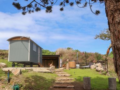 A shepherds hut on wheels with steps leading to a grassy area with a hot tub and lounge chairs at Bosulla Shepherds Hut in Penzance
