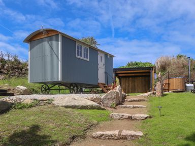 A shepherds hut on wheels with a wooden hot tub and stone steps in a garden at Bosulla Shepherds Hut in Penzance