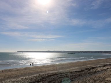 A beach with calm sea and two people with a dog walking near the shoreline at Bosulla Shepherds Hut in Penzance