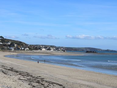 A sandy beach with a few people walking near the water and a village in the background at Bosulla Shepherds Hut in Penzance