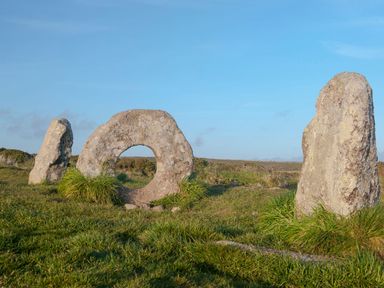 Three standing stones on grassy land under a blue sky at Bosulla Shepherds Hut in Penzance