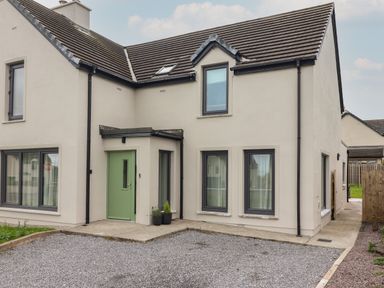 An exterior view of a two story house with a green front door and multiple windows at 19A Lighthouse Village Fenit County Kerry