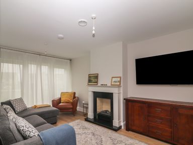 A living room with grey sofa and armchair near a fireplace and a wall mounted television at 19A Lighthouse Village in Fenit County Kerry