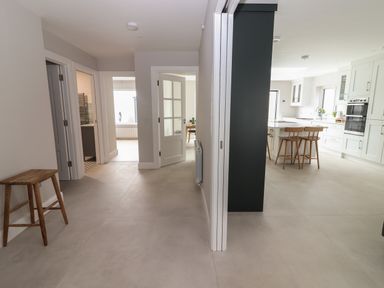 A hallway with a wooden stool and open doors leading to a kitchen with bar stools and a dining area at 19A Lighthouse Village in Fenit County Kerry