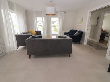 A living room with sofas chairs coffee table and sheer white curtains at 19A Lighthouse Village in Fenit County Kerry