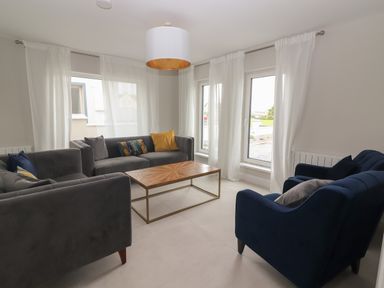 A living room with three sofas a wooden coffee table and white curtains at 19A Lighthouse Village in Fenit County Kerry
