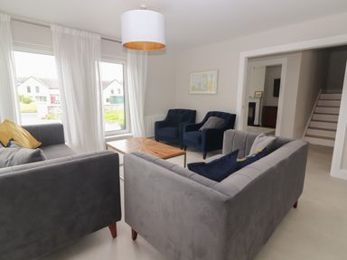 A sitting room with gray sofas navy armchairs a wooden coffee table and large windows at 19A Lighthouse Village in Fenit County Kerry