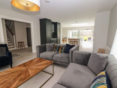 A living room with grey sofas and a wooden coffee table adjacent to an open kitchen with a dining area at 19A Lighthouse Village Fenit County Kerry