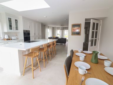 A kitchen and dining area with a white island and wooden chairs at 19A Lighthouse Village in Fenit County Kerry