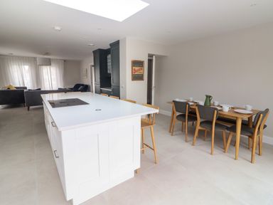 A kitchen with a white island and wooden chairs next to a dining table set with plates cups and a green jug at 19A Lighthouse Village in Fenit County Kerry