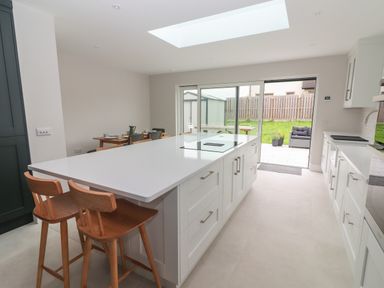 A kitchen with a large island and wooden stools next to sliding glass doors opening to a patio at 19A Lighthouse Village in Fenit County Kerry