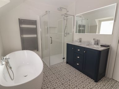 A bathroom with a freestanding bathtub glass shower double sink vanity and patterned floor tiles at 19A Lighthouse Village in Fenit County Kerry