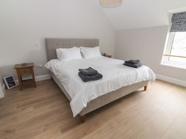 A bedroom with a bed with white bedding two bedside tables and a window at 19A Lighthouse Village in Fenit County Kerry