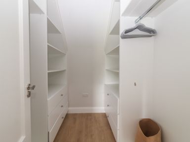 A walk in closet with white shelves drawers a wooden floor and a basket at 19A Lighthouse Village in Fenit County Kerry