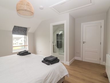 A bedroom with a bed with folded towels on it a window with a patterned roller blind an open door leading to a bathroom and a closed white door at 19A Lighthouse Village in Fenit County Kerry