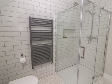A bathroom with a glass shower enclosure a gray towel radiator and white tiled walls at 19A Lighthouse Village in Fenit County Kerry