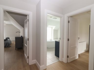 A hallway with three open doors showing a bedroom a bathroom with a bathtub and a room with a radiator at 19A Lighthouse Village in Fenit County Kerry