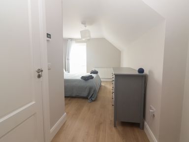 A bedroom with a bed covered by a blanket and towels a grey dresser and a window with curtains at 19A Lighthouse Village in Fenit County Kerry