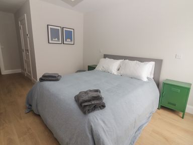 A bedroom with a bed covered in a gray blanket and white pillows next to green bedside cabinets at 19A Lighthouse Village in Fenit County Kerry