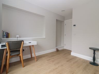 A room with a wooden floor a white desk and chair books on a shelf and a small round table at 19A Lighthouse Village in Fenit County Kerry