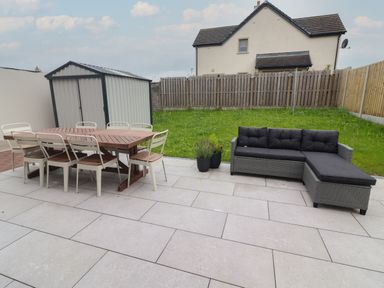 A backyard patio with a wooden dining table and six chairs a storage shed a wicker sectional sofa and some potted plants at 19A Lighthouse Village in Fenit County Kerry