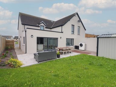 A backyard with a patio containing a sofa and a dining table with chairs and a grassy lawn at 19A Lighthouse Village in Fenit County Kerry
