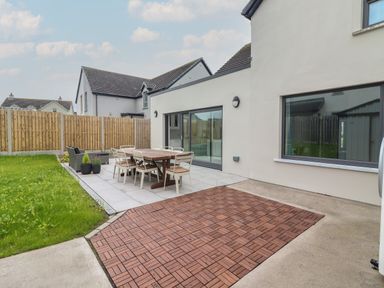 An outdoor patio area with a dining table and chairs a grass lawn and a wooden fence at 19A Lighthouse Village in Fenit County Kerry