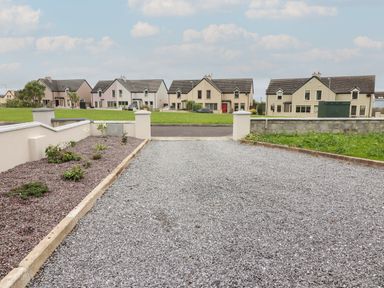 A gravel driveway and garden area with houses and a grassy area in the background at 19A Lighthouse Village in Fenit County Kerry