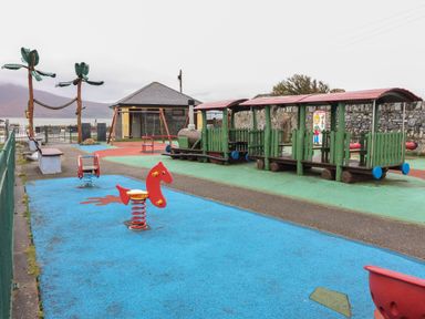 An outdoor playground with a spring horse rider a green train play structure and swing set at 19A Lighthouse Village in Fenit County Kerry