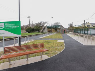 An outdoor pathway with benches bike racks and a sign welcoming to the kingdom of kerry greenways at 19A Lighthouse Village in Fenit County Kerry