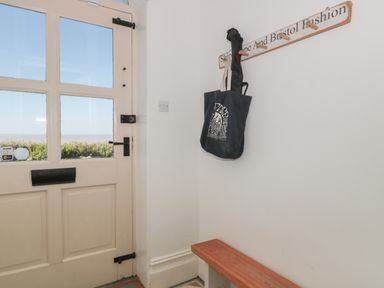 A corner entryway with a wooden bench a wall-mounted coat rack holding bags and an umbrella and a door with glass panels at 49 Esplanade in Burnham-On-Sea