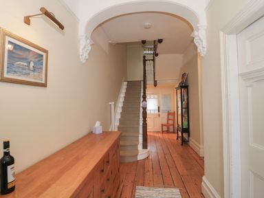A hallway with wooden floorboards a staircase a wooden cabinet a framed picture and a glass display case at 49 Esplanade in Burnham-On-Sea