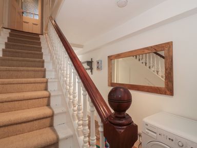 A staircase with carpeted steps and wooden banister next to a washing machine and a wall mirror at 49 Esplanade in Burnham-On-Sea